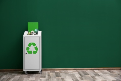 Photo of Overfilled trash bin with recycling symbol near color wall indoors. Space for text