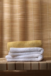 Photo of Stacked soft towels on wicker bench indoors