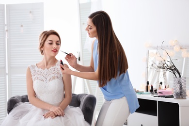 Photo of Makeup artist preparing bride before her wedding in room