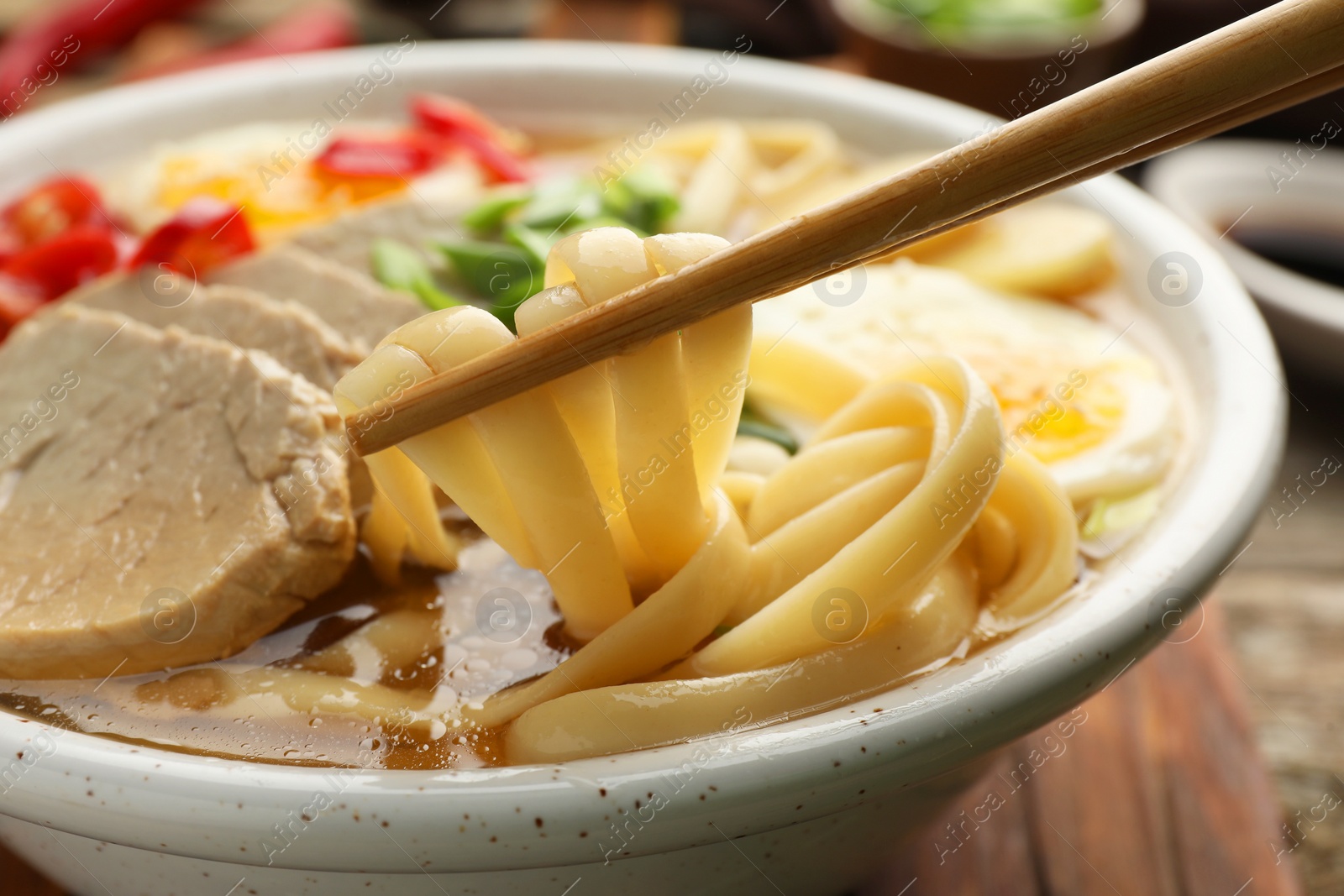 Photo of Eating delicious ramen with chopsticks at table, closeup. Noodle soup