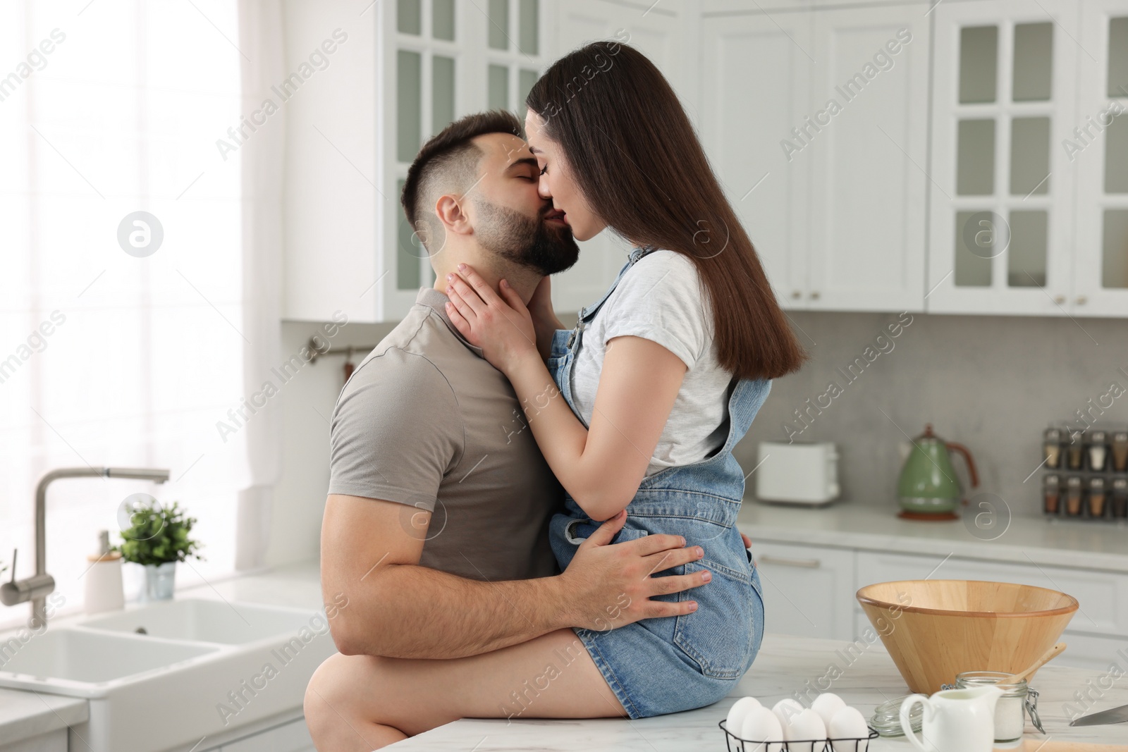 Photo of Affectionate young couple kissing in light kitchen