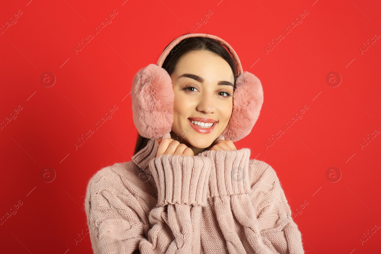 Photo of Beautiful young woman wearing earmuffs on red background