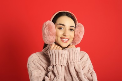 Beautiful young woman wearing earmuffs on red background