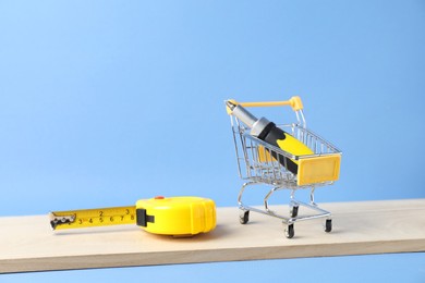 Photo of Small shopping cart with set of construction tools on light blue background. Space for text