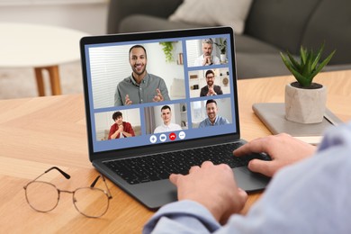 Image of Man having video chat with coworkers via laptop at wooden table, closeup
