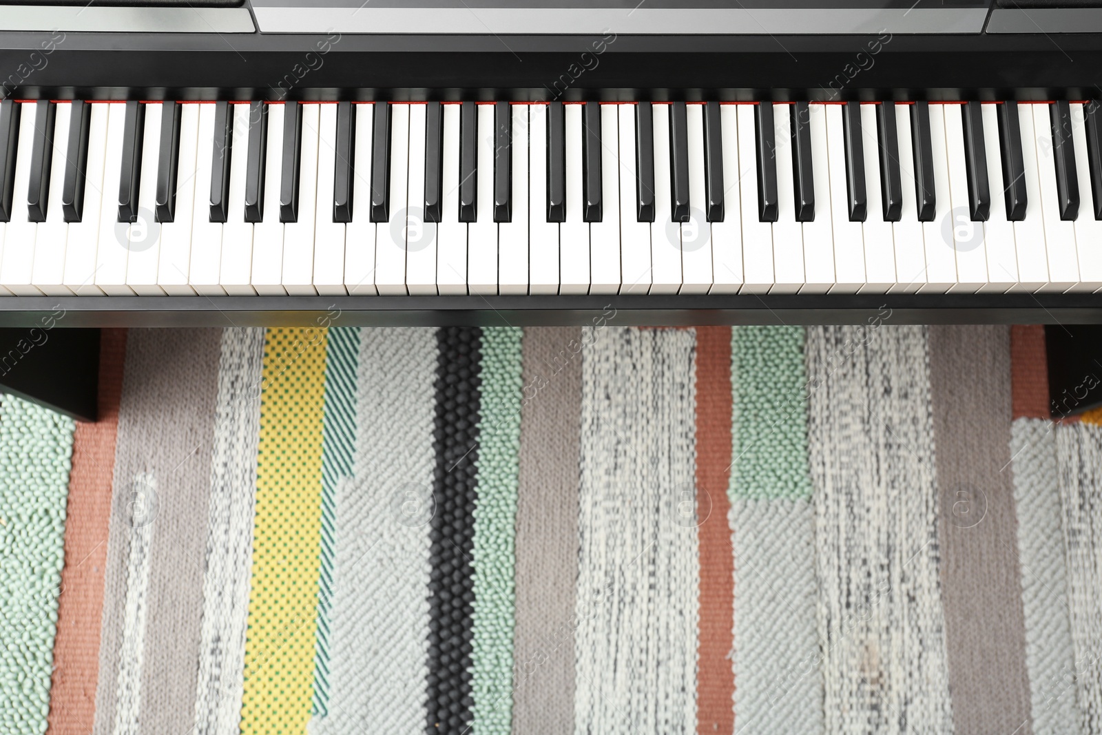 Photo of Modern piano with black and white keys over rug, top view. Space for text