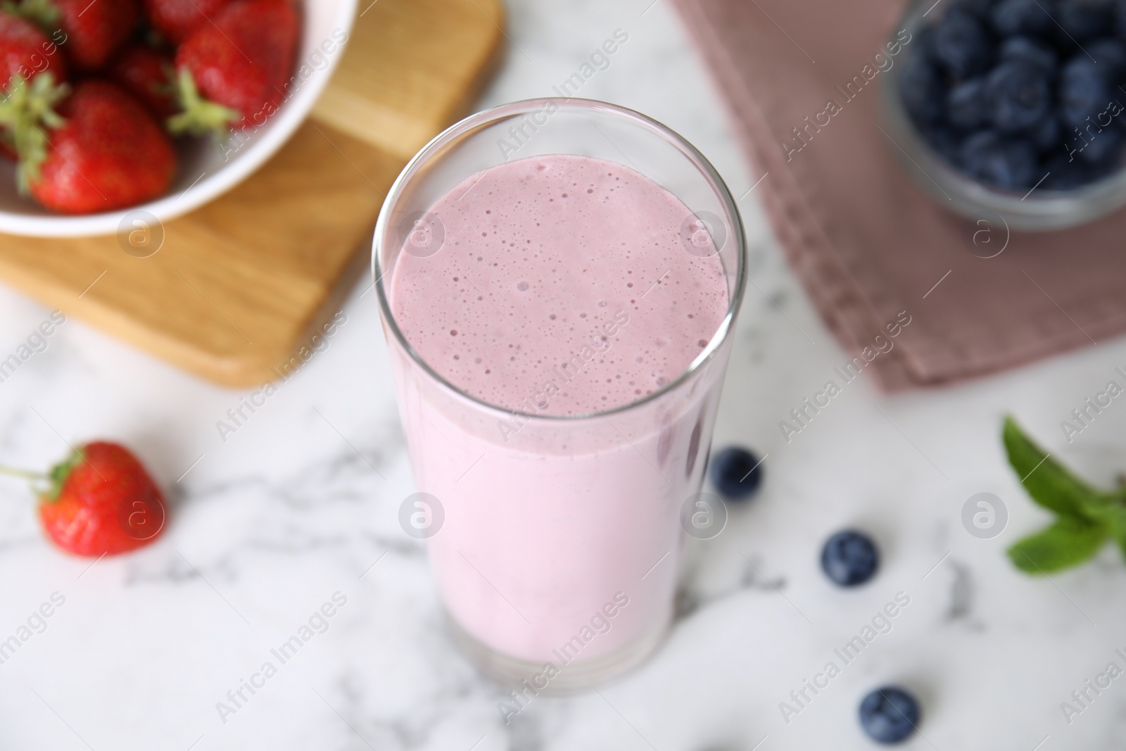 Photo of Tasty milk shake and berries on light table, closeup