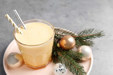 Photo of Glass of delicious eggnog and decorated fir branch on gray table