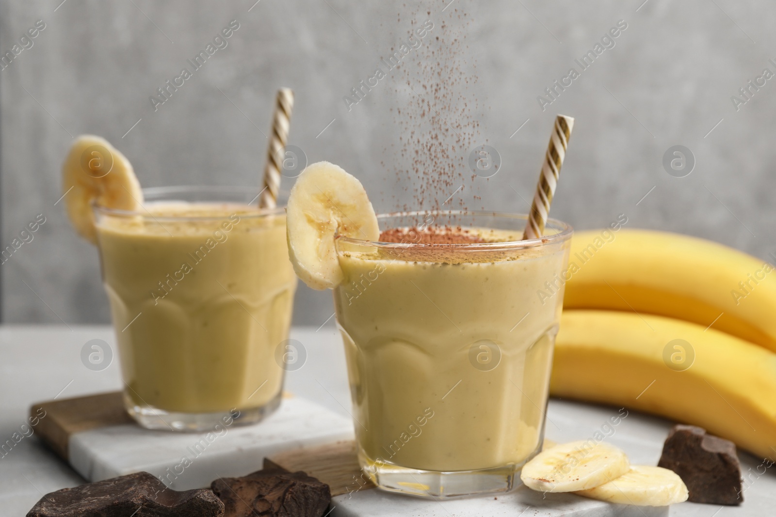 Photo of Sprinkling chocolate powder onto tasty banana smoothie on white table