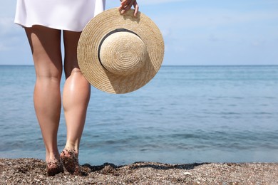 Woman with straw hat near water at beach, closeup. Space for text