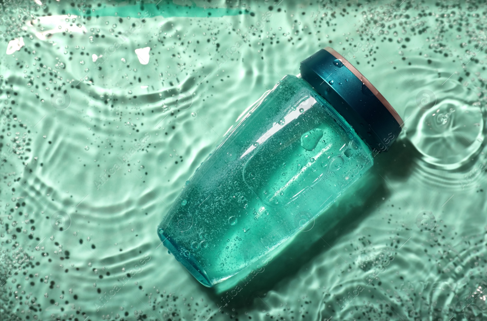 Photo of Bottle of hair care cosmetic product in water on turquoise background, top view