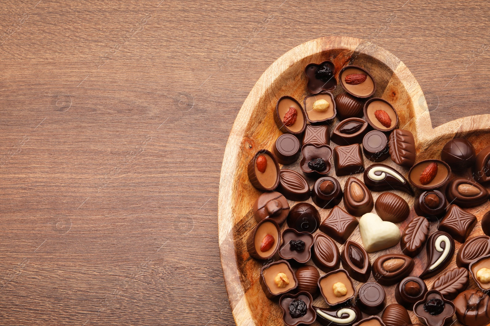 Photo of Heart shaped plate with delicious chocolate candies on wooden table, top view. Space for text