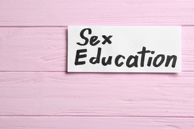 Photo of Piece of paper with phrase "SEX EDUCATION" on pink wooden background, top view