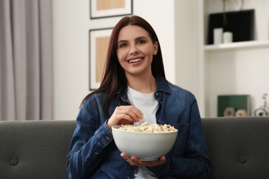 Photo of Happy woman with bowl of popcorn watching TV at home