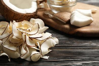 Pile of tasty coconut chips on black wooden table. Space for text