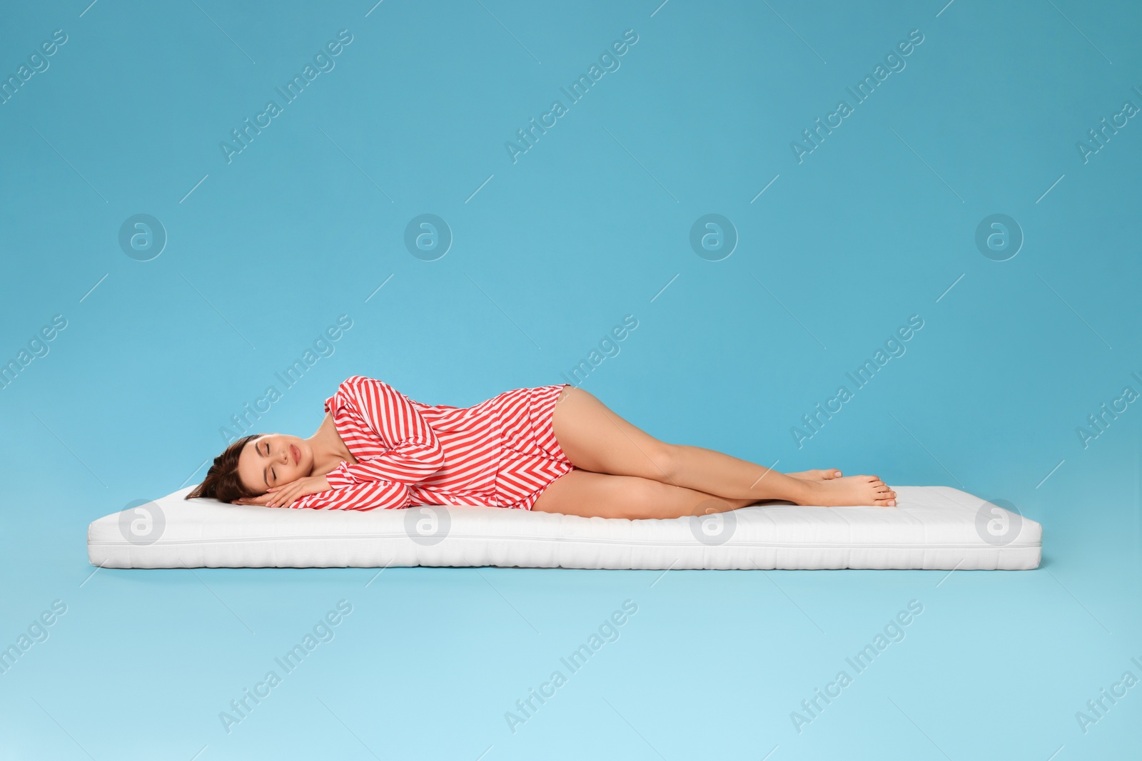 Photo of Young woman sleeping on soft mattress against light blue background