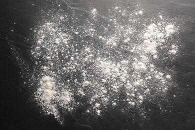 Photo of Scattered flour on black textured table, top view