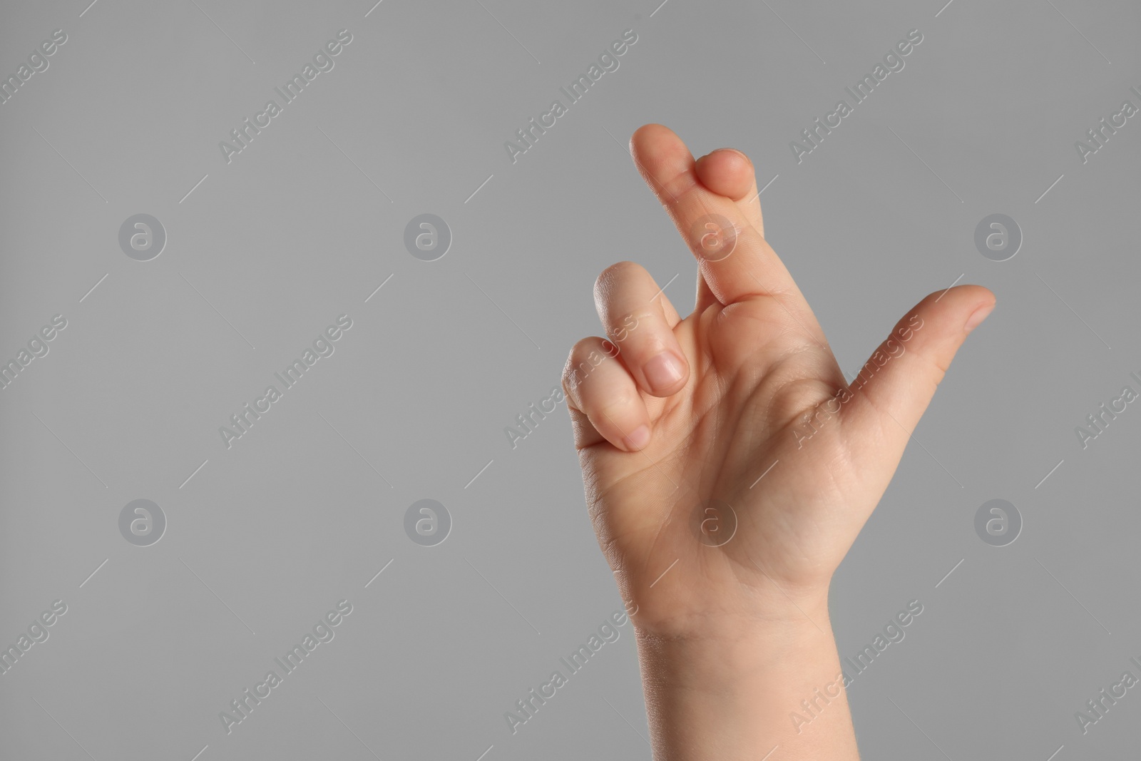 Photo of Child holding fingers crossed on light grey background, closeup with space for text. Good luck superstition