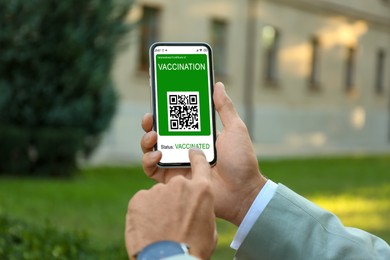 Man holding smartphone with international certificate of vaccination outdoors, closeup