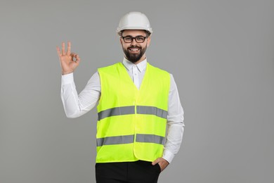 Photo of Engineer in hard hat showing ok gesture on grey background