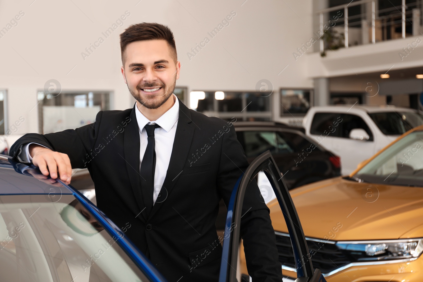 Photo of Young salesman near new car in dealership