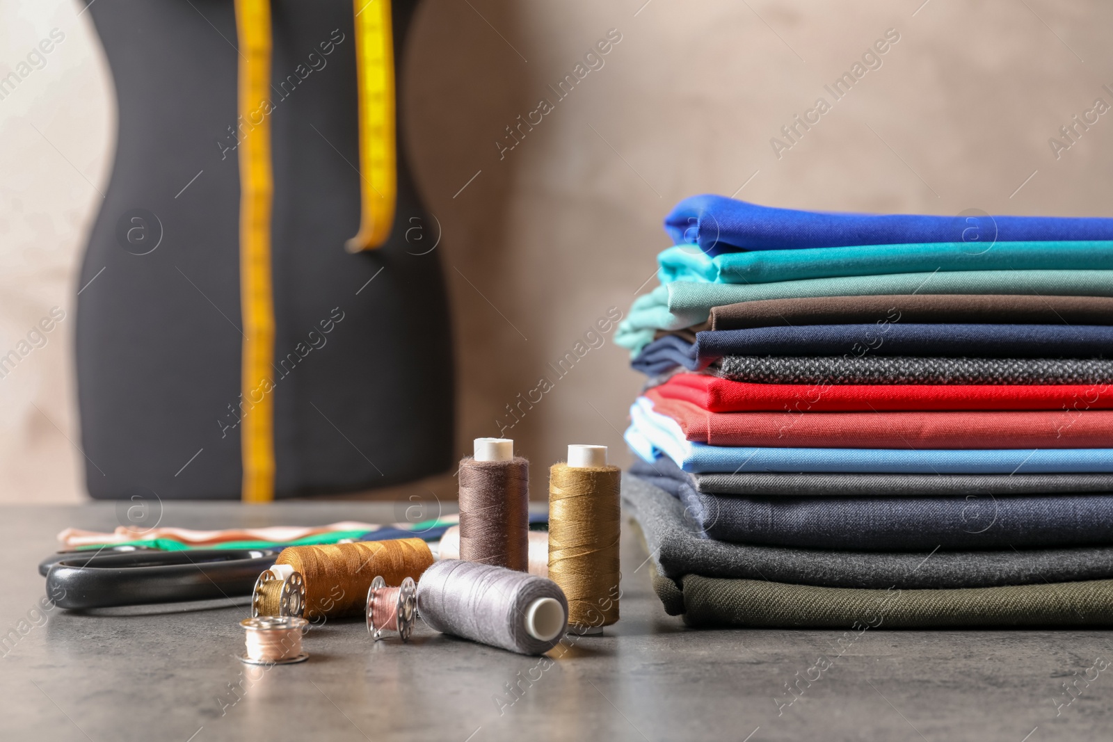 Photo of Bobbins with threads and stack of colorful fabrics on table. Tailoring accessories