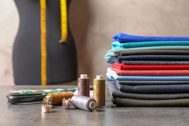 Photo of Bobbins with threads and stack of colorful fabrics on table. Tailoring accessories