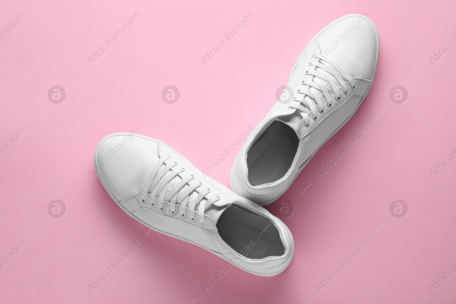 Photo of Pair of stylish white sneakers on pink background, top view