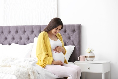 Young beautiful pregnant woman sitting on bed and touching her belly at home