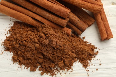 Dry aromatic cinnamon sticks and powder on white wooden table, top view