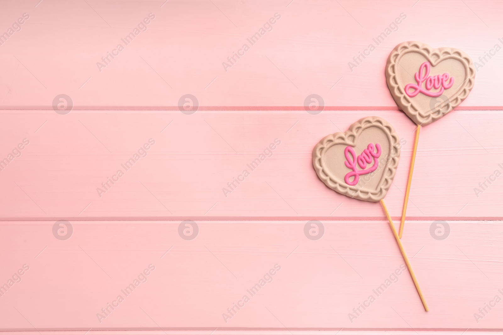 Photo of Chocolate heart shaped lollipops with word Love on pink wooden table, flat lay. Space for text