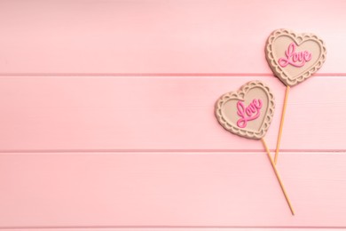 Chocolate heart shaped lollipops with word Love on pink wooden table, flat lay. Space for text