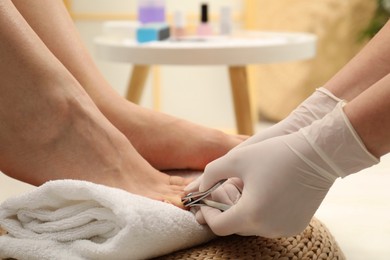 Professional pedicurist cutting client`s toenails with clipper in beauty salon, closeup