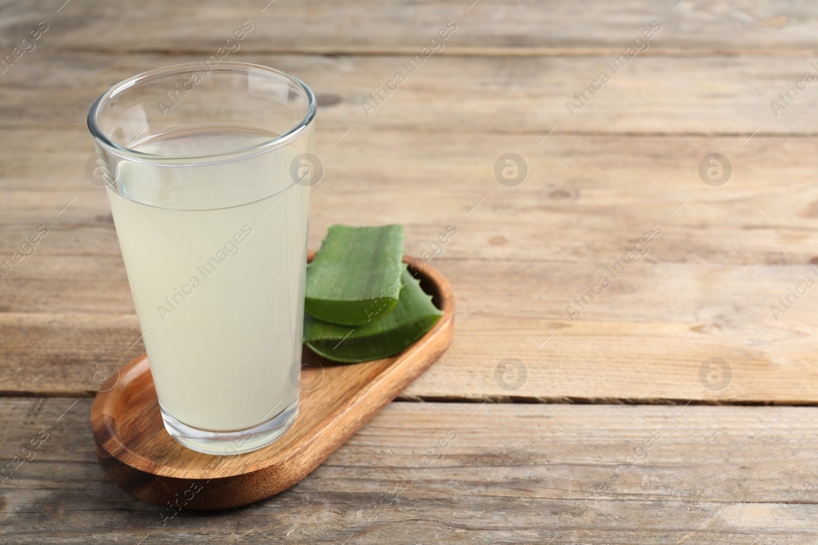 Photo of Tasty aloe juice in glass and cut fresh leaves on wooden table, closeup. Space for text