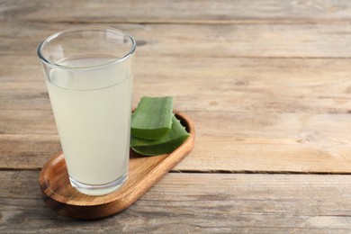 Photo of Tasty aloe juice in glass and cut fresh leaves on wooden table, closeup. Space for text