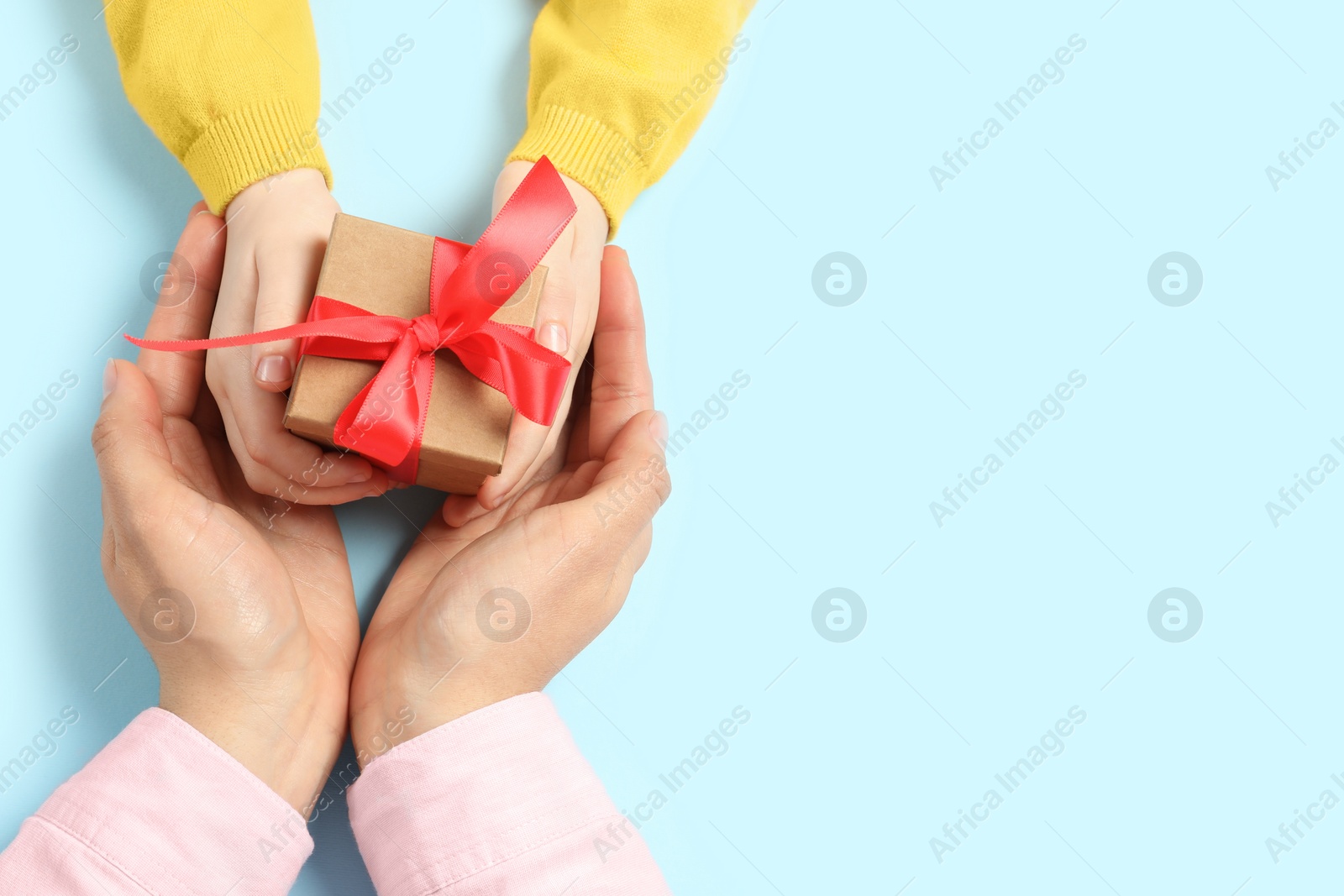 Photo of Mother giving gift box to her child on light blue background, top view. Space for text