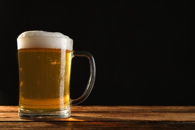 Cold tasty beer on wooden table against dark background. Space for text