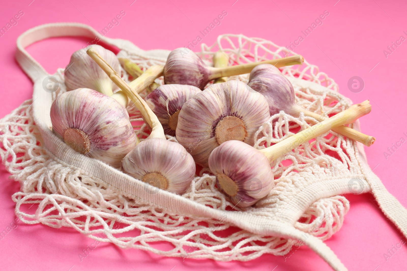 Photo of String bag with garlic heads on bright pink background, closeup