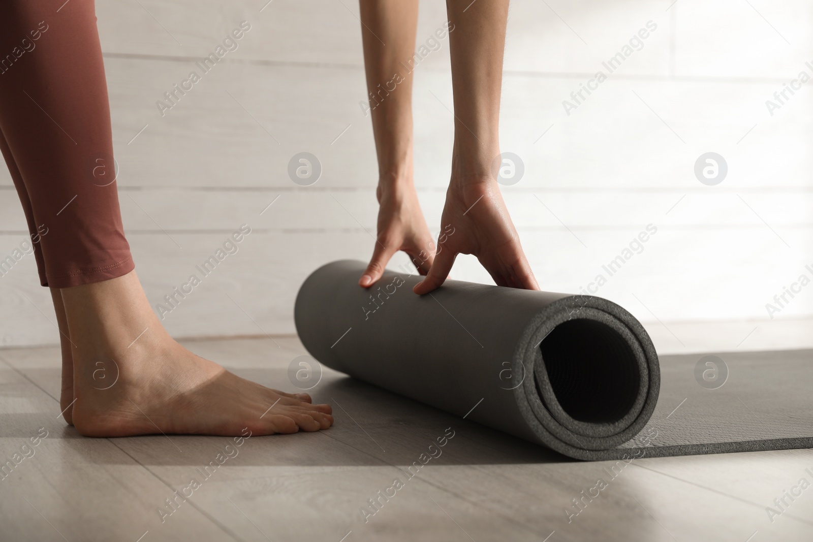 Photo of Woman rolling black yoga mat on floor indoors, closeup