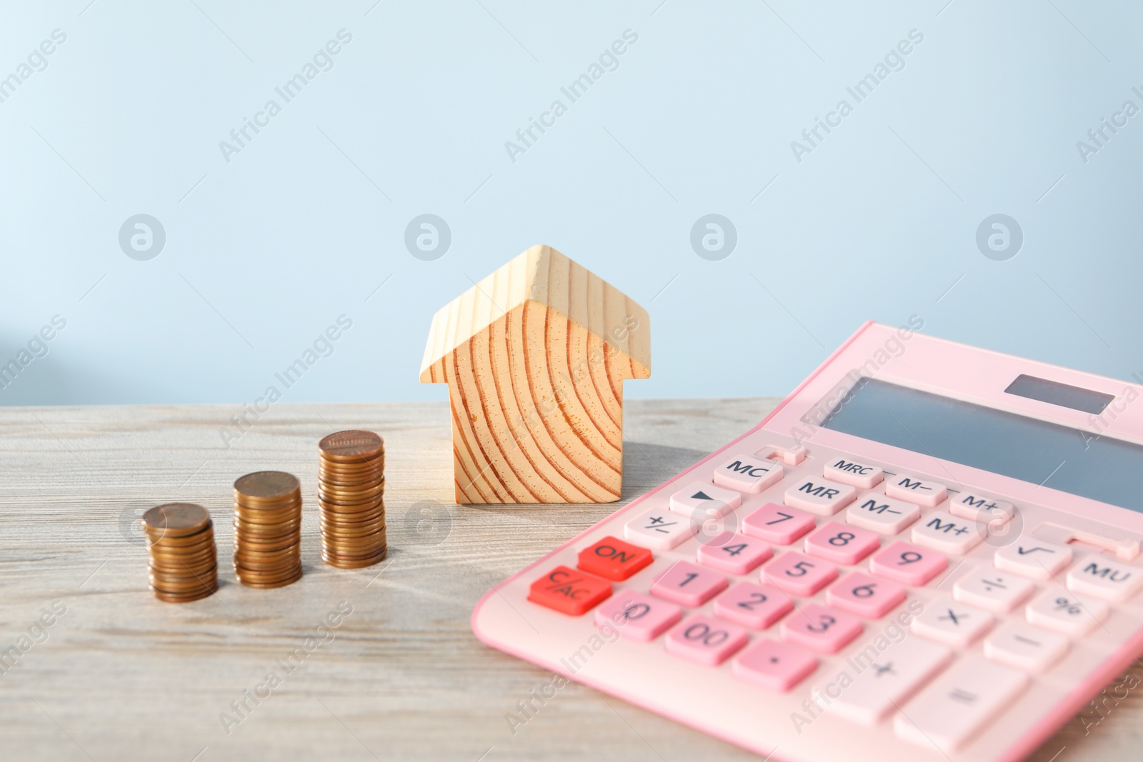 Photo of House model, calculator and coins on wooden table against light blue background