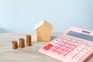 Photo of House model, calculator and coins on wooden table against light blue background