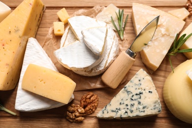 Different delicious cheeses served on wooden board, above view