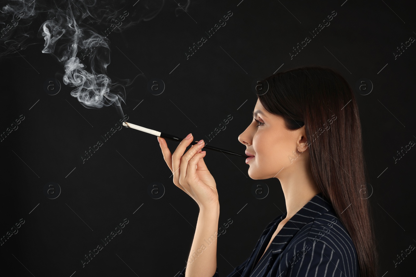 Photo of Woman using long cigarette holder for smoking on black background