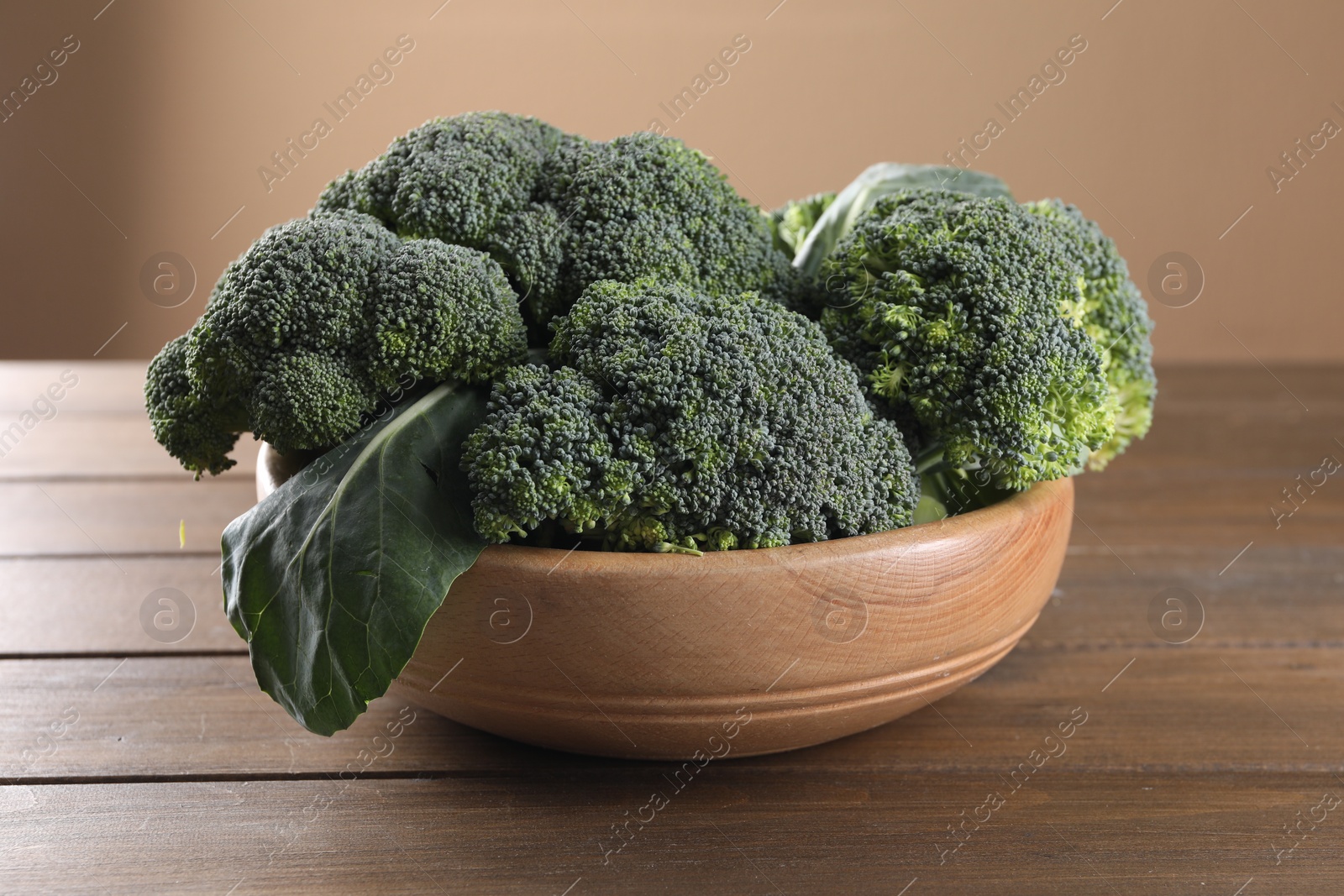 Photo of Bowl with fresh raw broccoli on wooden table, closeup