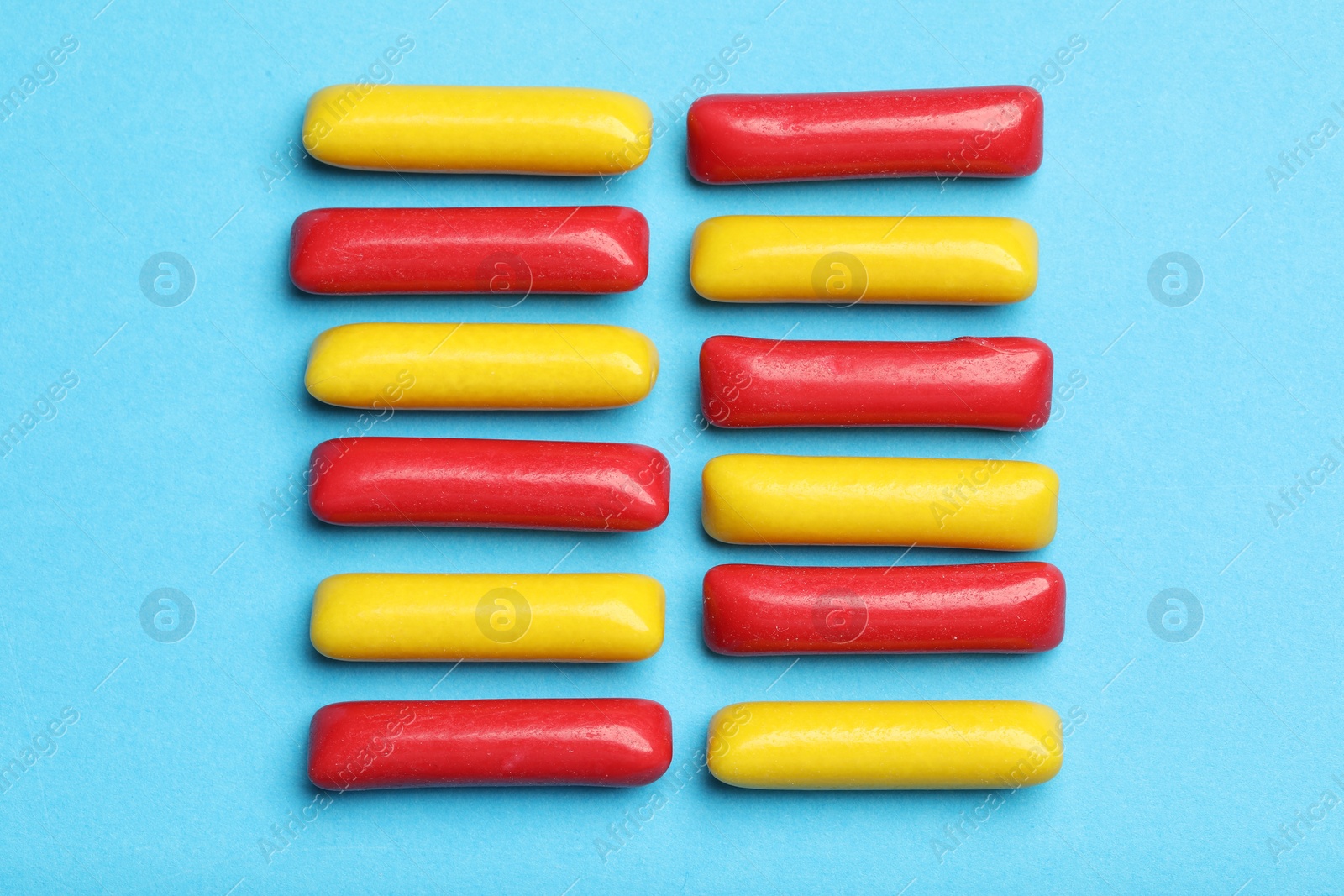 Photo of Many tasty bubble gums on light blue background, flat lay