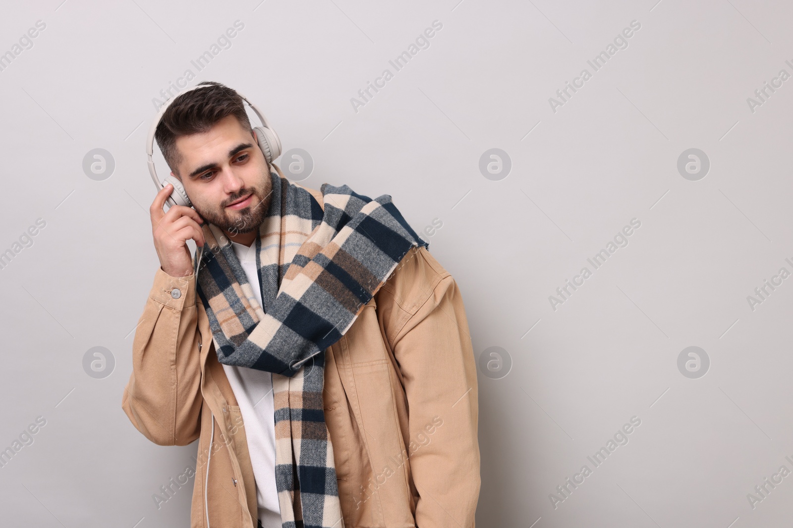 Photo of Handsome man in warm scarf listening to music on light grey background. Space for text