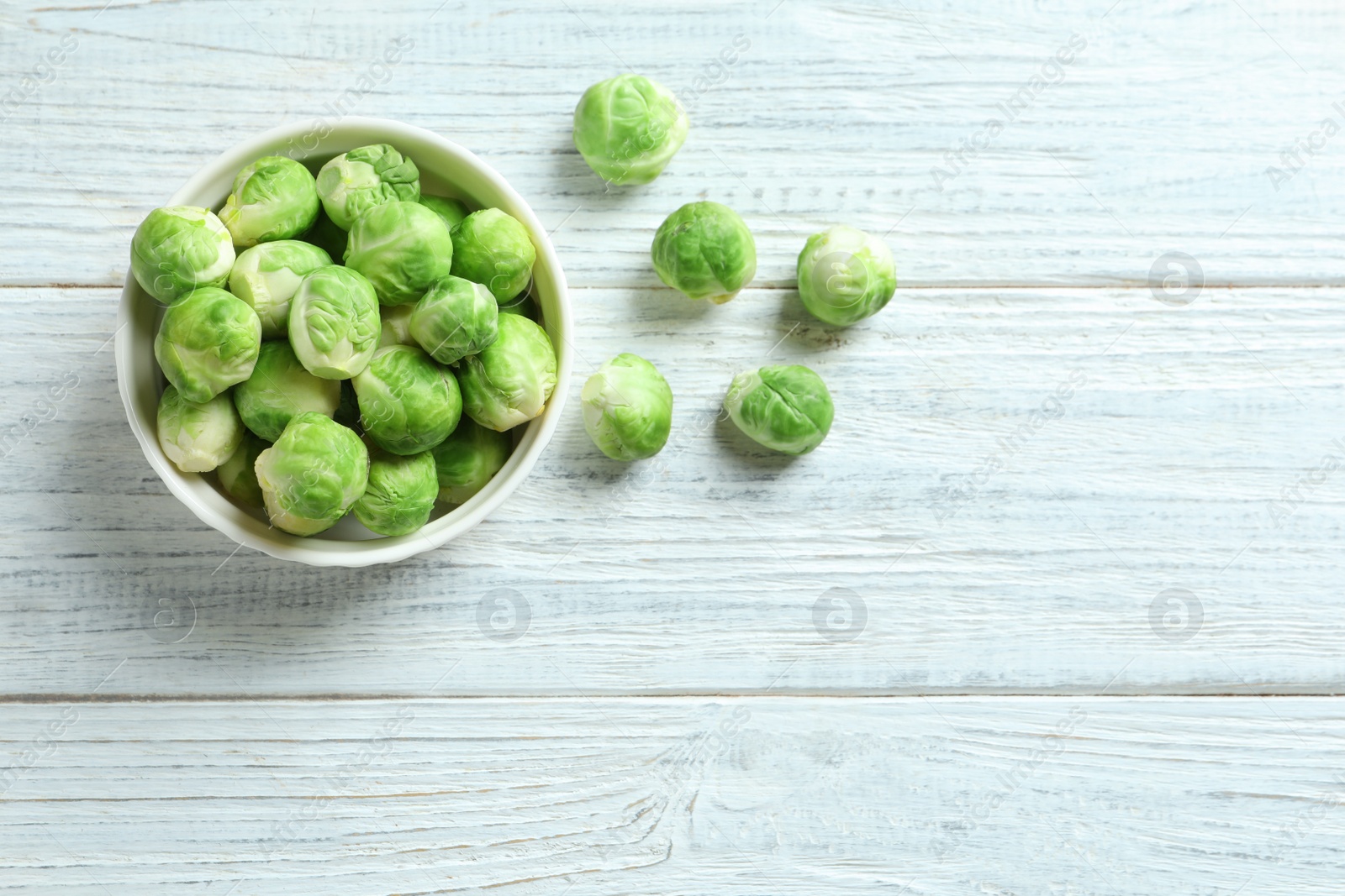 Photo of Bowl of fresh Brussels sprouts and space for text on wooden background, top view