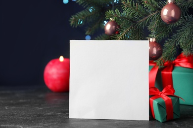 Blank greeting card and gift boxes near Christmas tree on table against dark background, closeup. Space for text