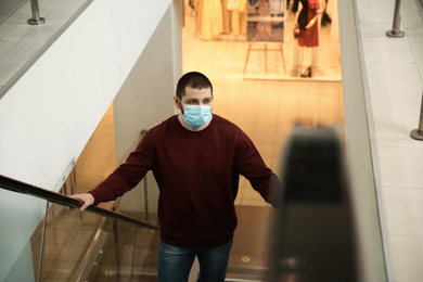 Photo of Man with disposable mask on escalator in mall. Dangerous virus