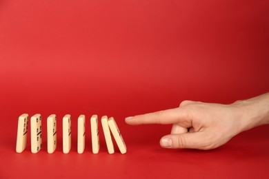 Woman causing chain reaction by pushing domino tile on red background, closeup. Space for text